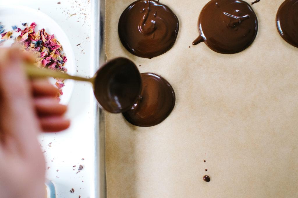 melted dark chocolate being drizzled onto parchment paper for mendiants