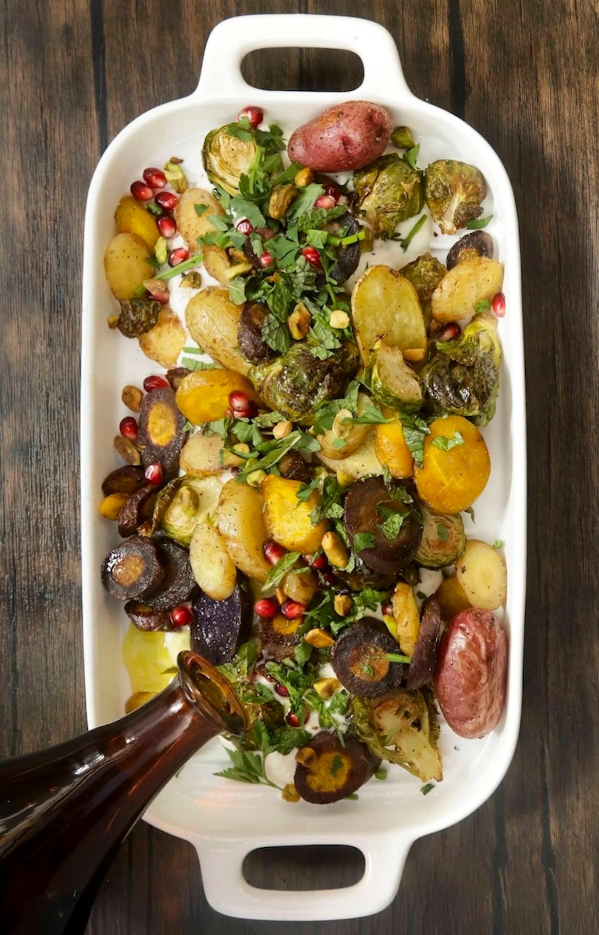 Person drizzling bright green herb oil over a tray of hot roasted vegetables fresh out of the oven
