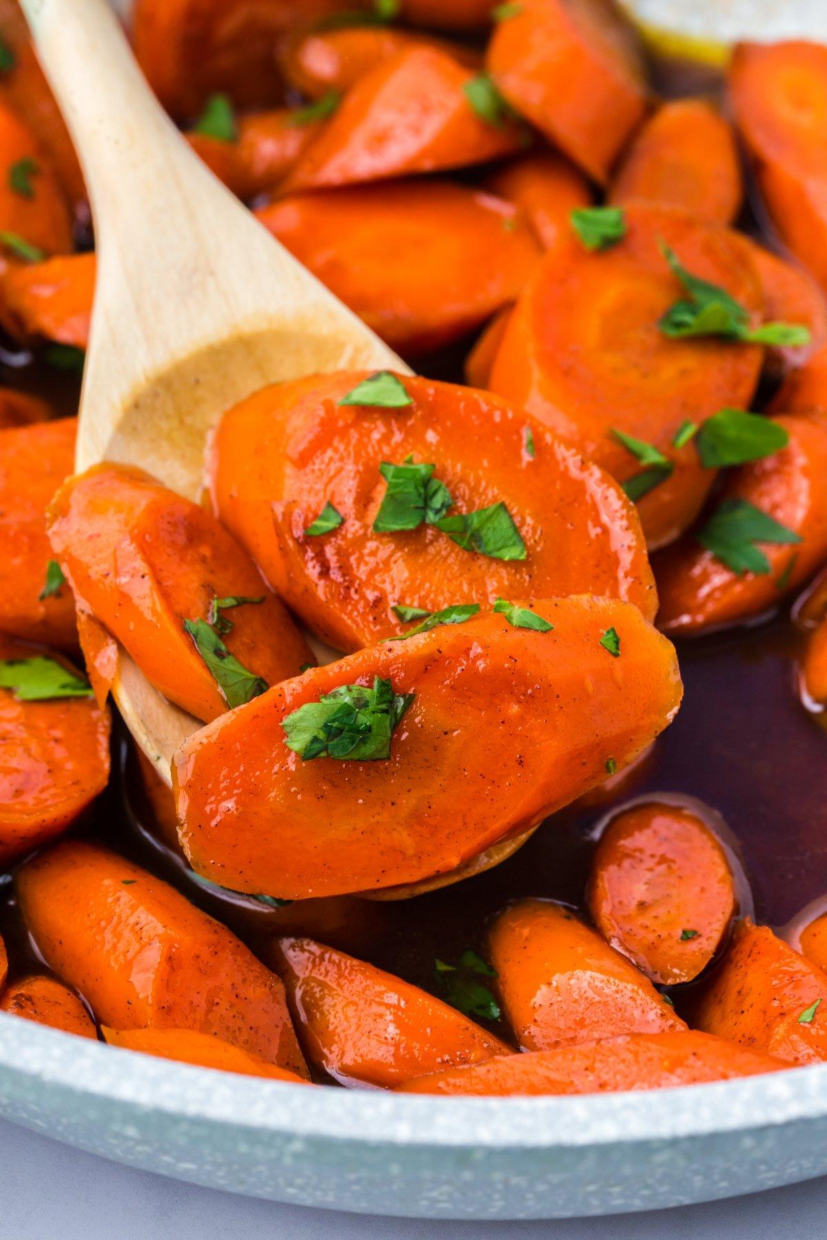 serving spoon scooping honey glazed carrots from a skillet into a white bowl