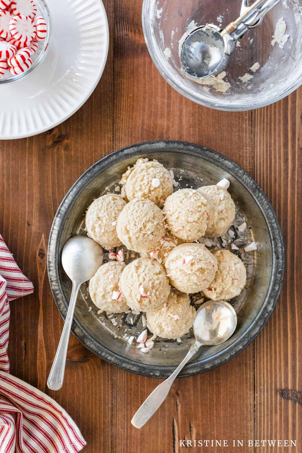 Bowl of peppermint chocolate cookie dough, with a spoon for scooping, next to a plate of powdered sugar.
