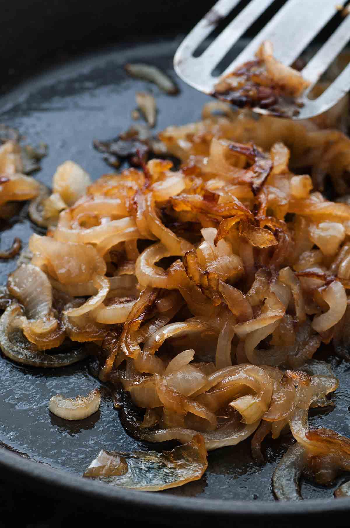 close-up shot of thinly sliced onions caramelizing slowly in a skillet