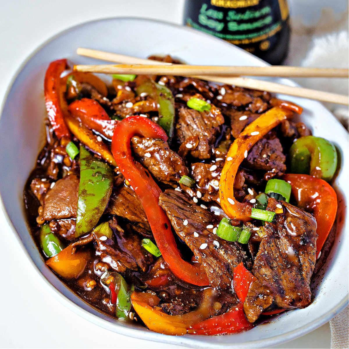 Sizzling flank steak being stir-fried in a wok with chili glaze