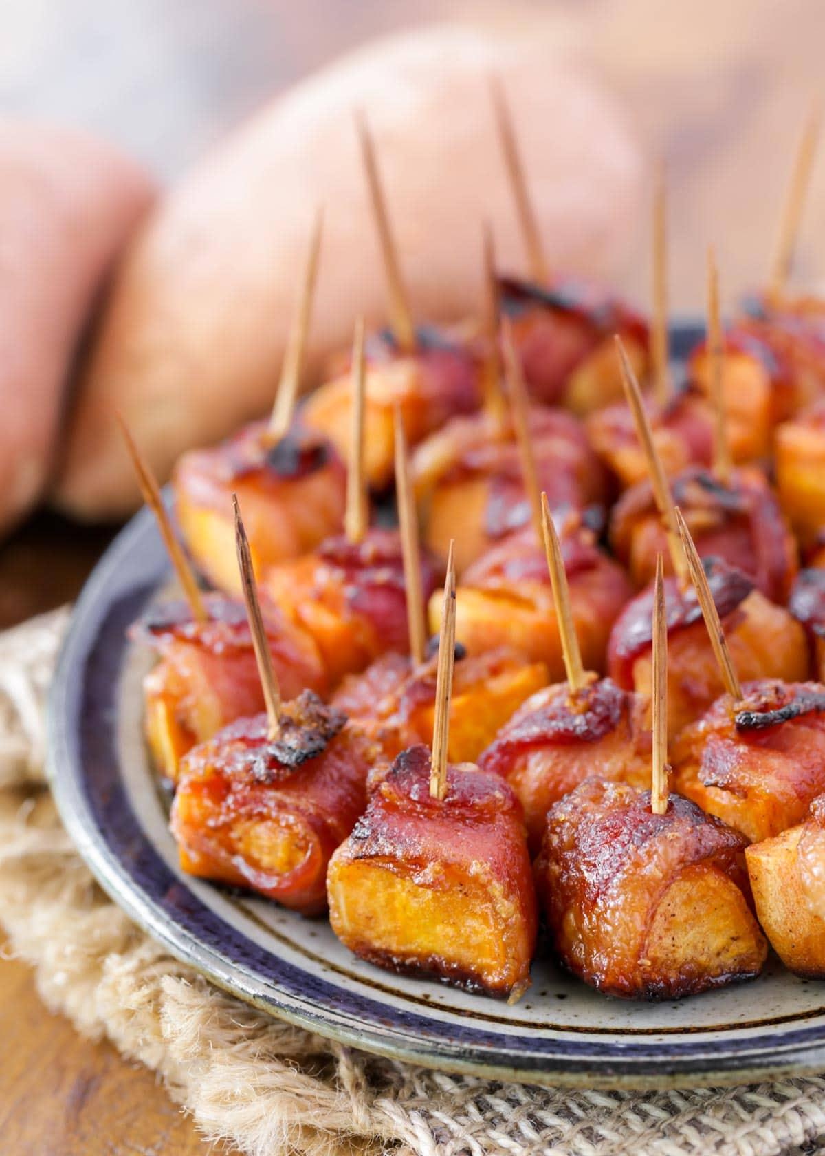 close-up of raw sweet potato cubes being wrapped with bacon strips