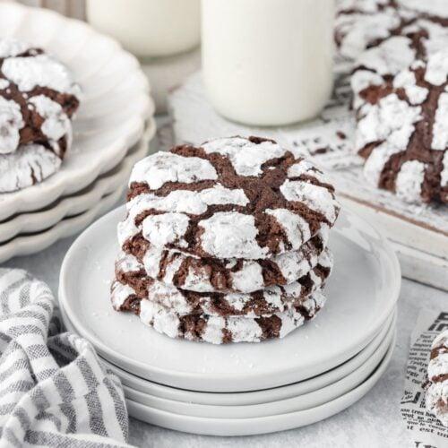 Plate of freshly baked chocolate crinkle cookies with powdered sugar and visible cracks, cozy kitchen background, warm lighting