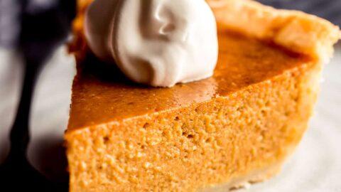 A homemade pumpkin pie looking a bit deflated and sad on a kitchen counter, with a hand gently patting it