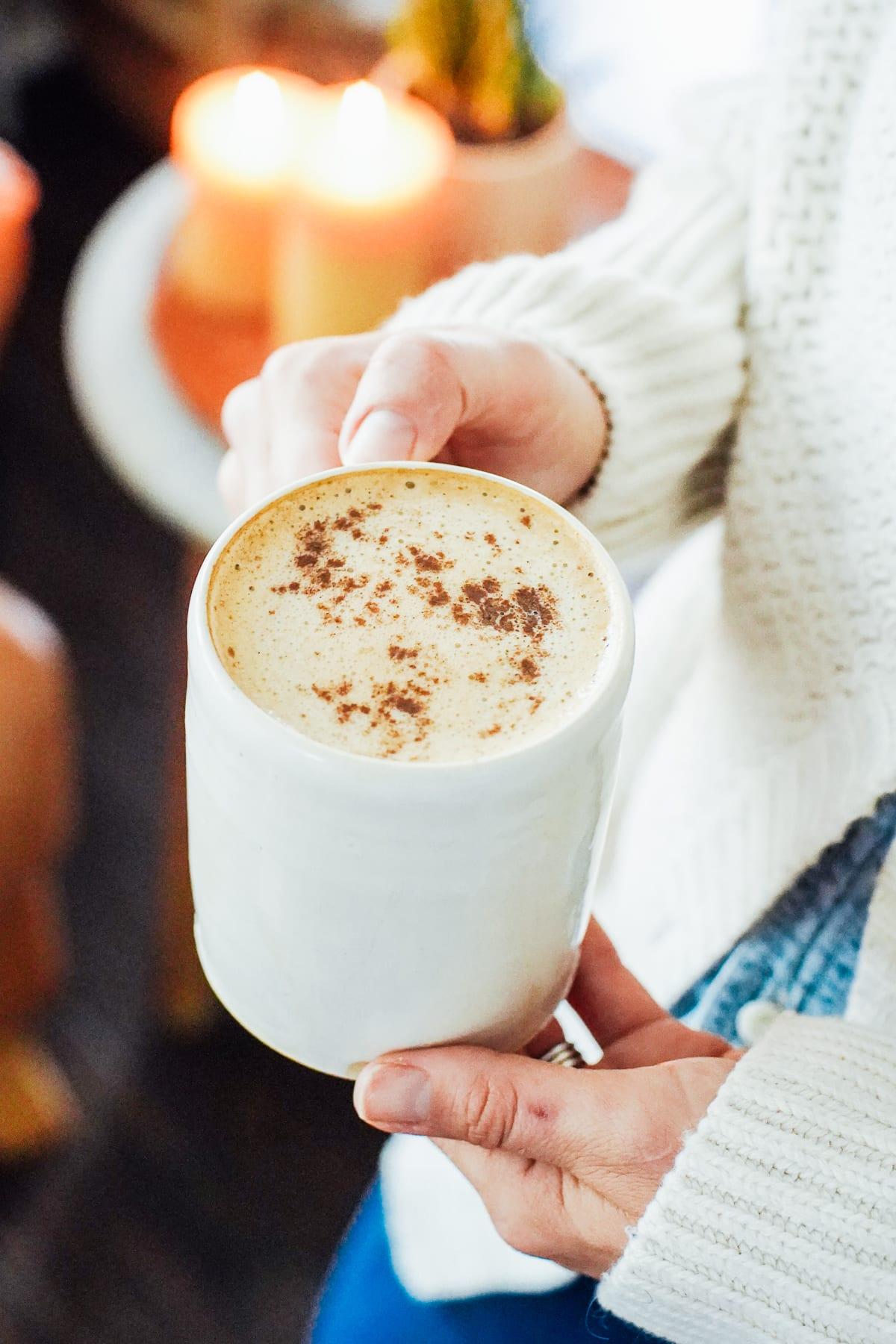 Hands holding a warm mug of pumpkin spice latte next to a slice of pumpkin cheesecake
