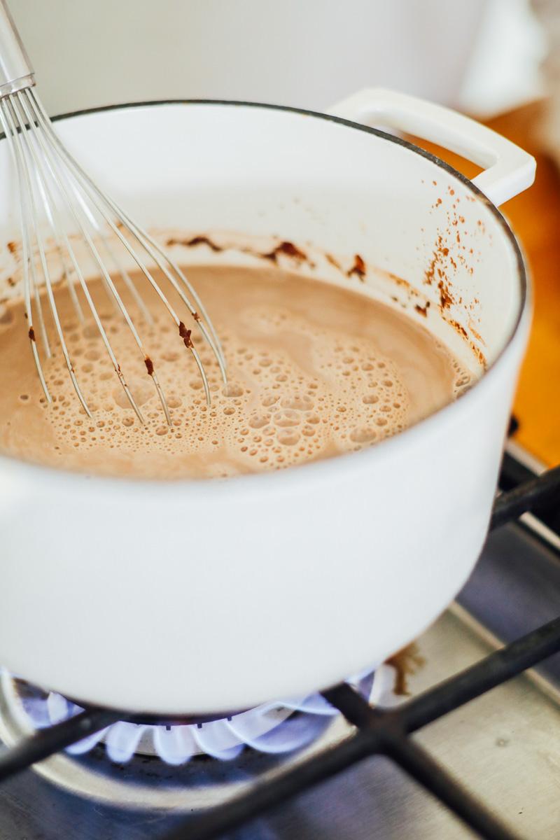 hand whisking almond milk and cocoa powder in a saucepan on a stovetop