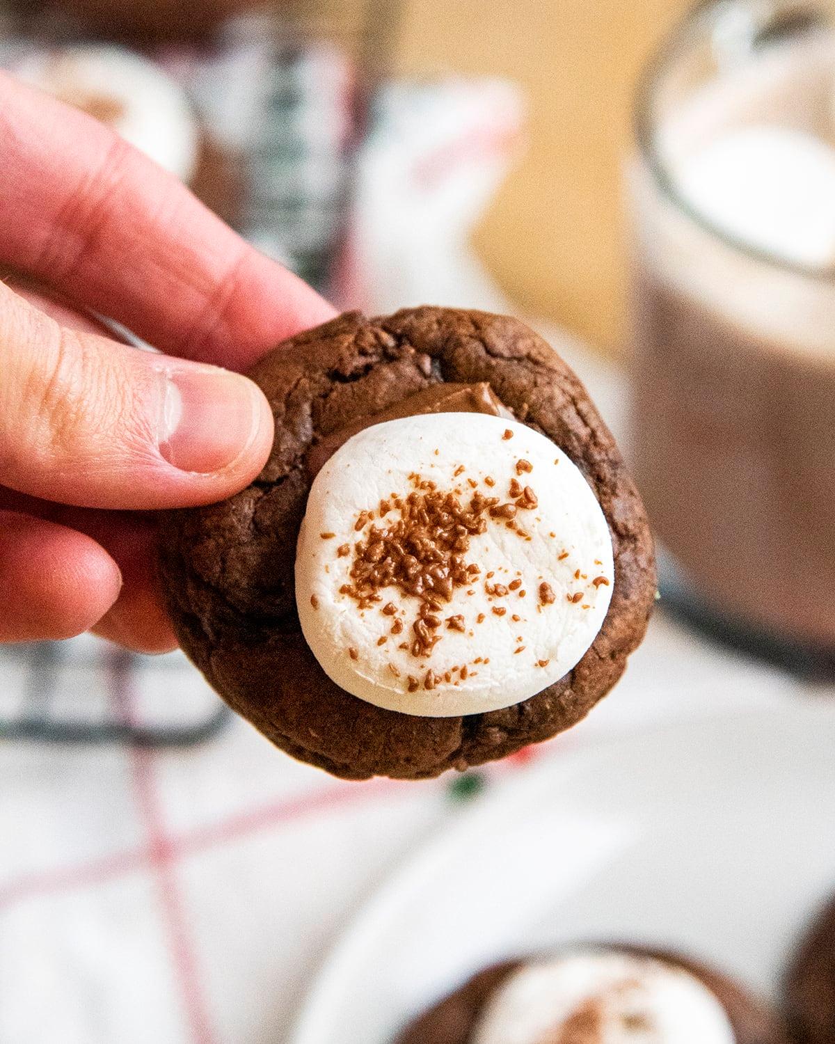 Hand holding a freshly baked cocoa cookie, showing its soft interior and white drizzle