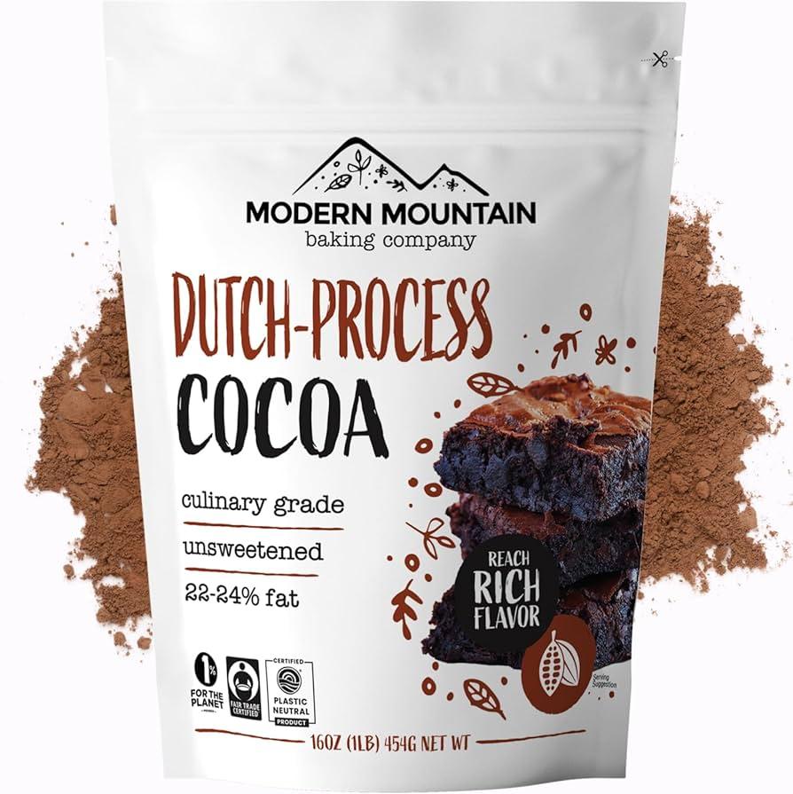 Close-up of high-quality unsweetened Dutch-processed cocoa powder, chopped dark chocolate, and a vanilla bean on a rustic wooden cutting board