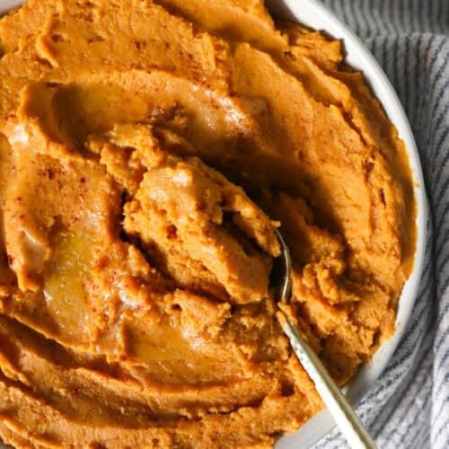 serving spoon scooping creamy sweet potato mash into a decorative bowl
