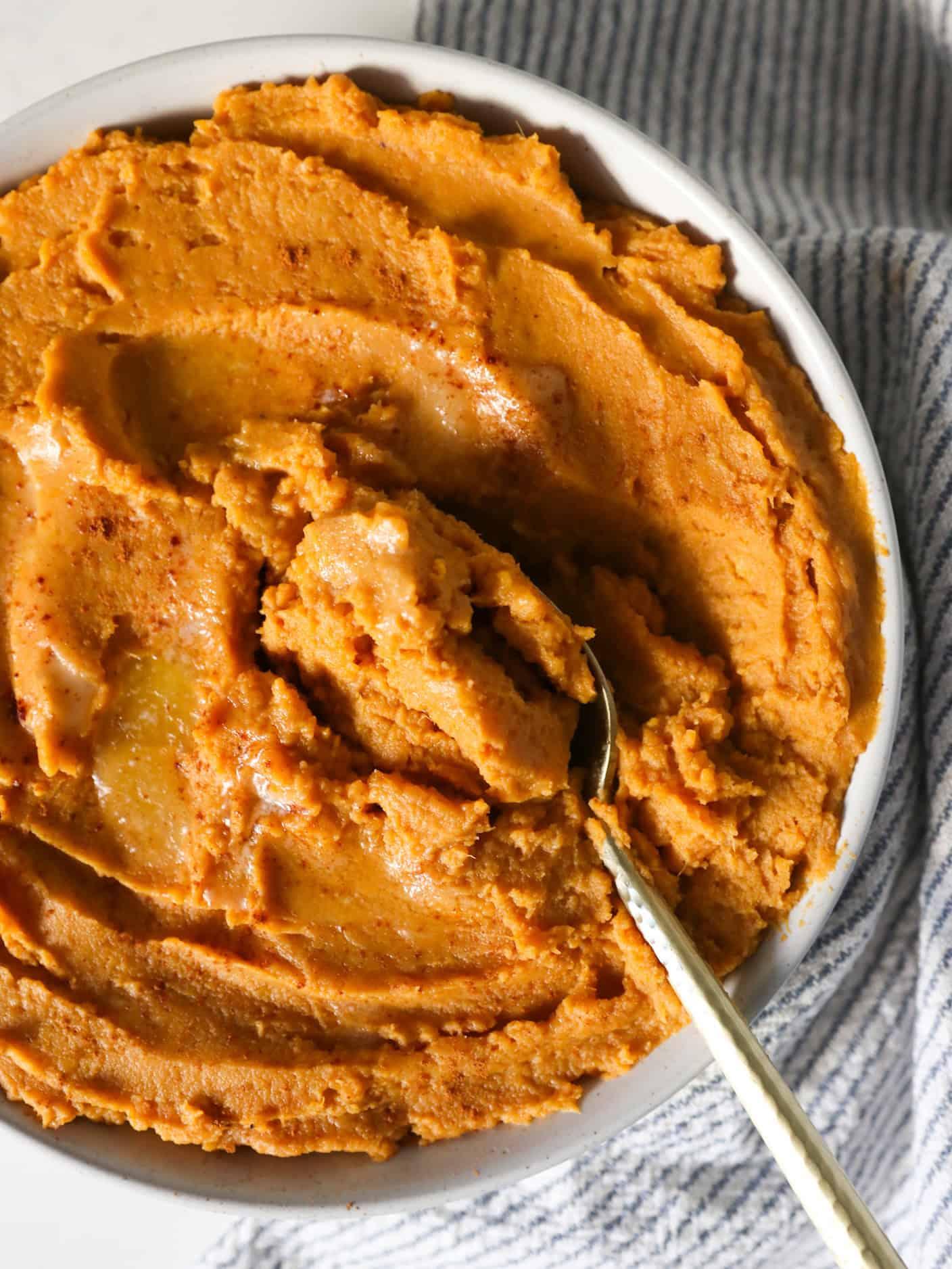 Close-up shot of creamy mashed sweet potatoes in a bowl, ready for casserole assembly, with spices and butter nearby