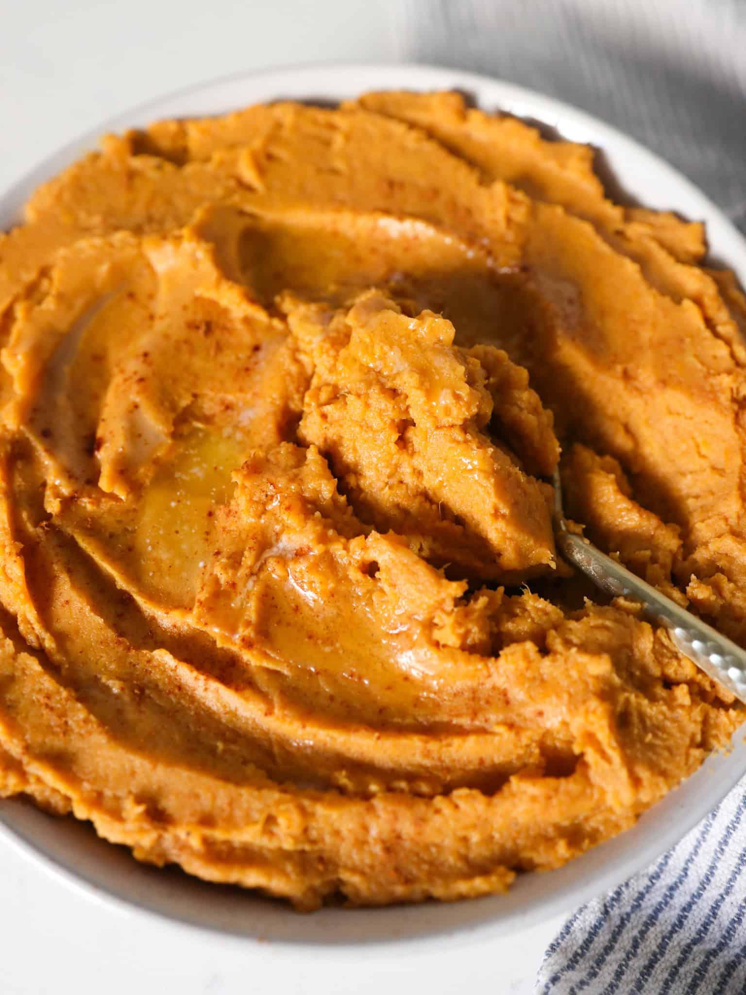 Close-up of creamy mashed sweet potatoes in a bowl, with cinnamon and nutmeg