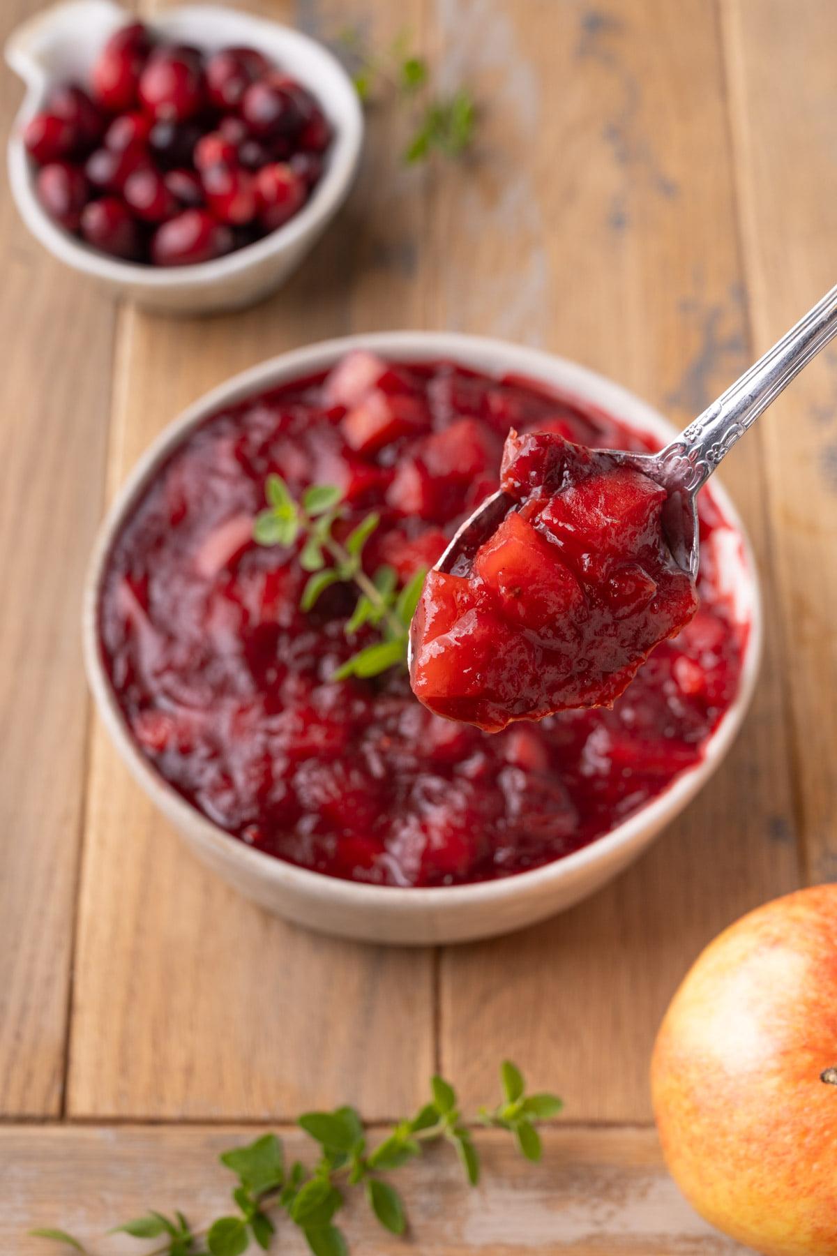 Close-up of a spoon scooping homemade cranberry sauce with visible apple chunks from a bowl