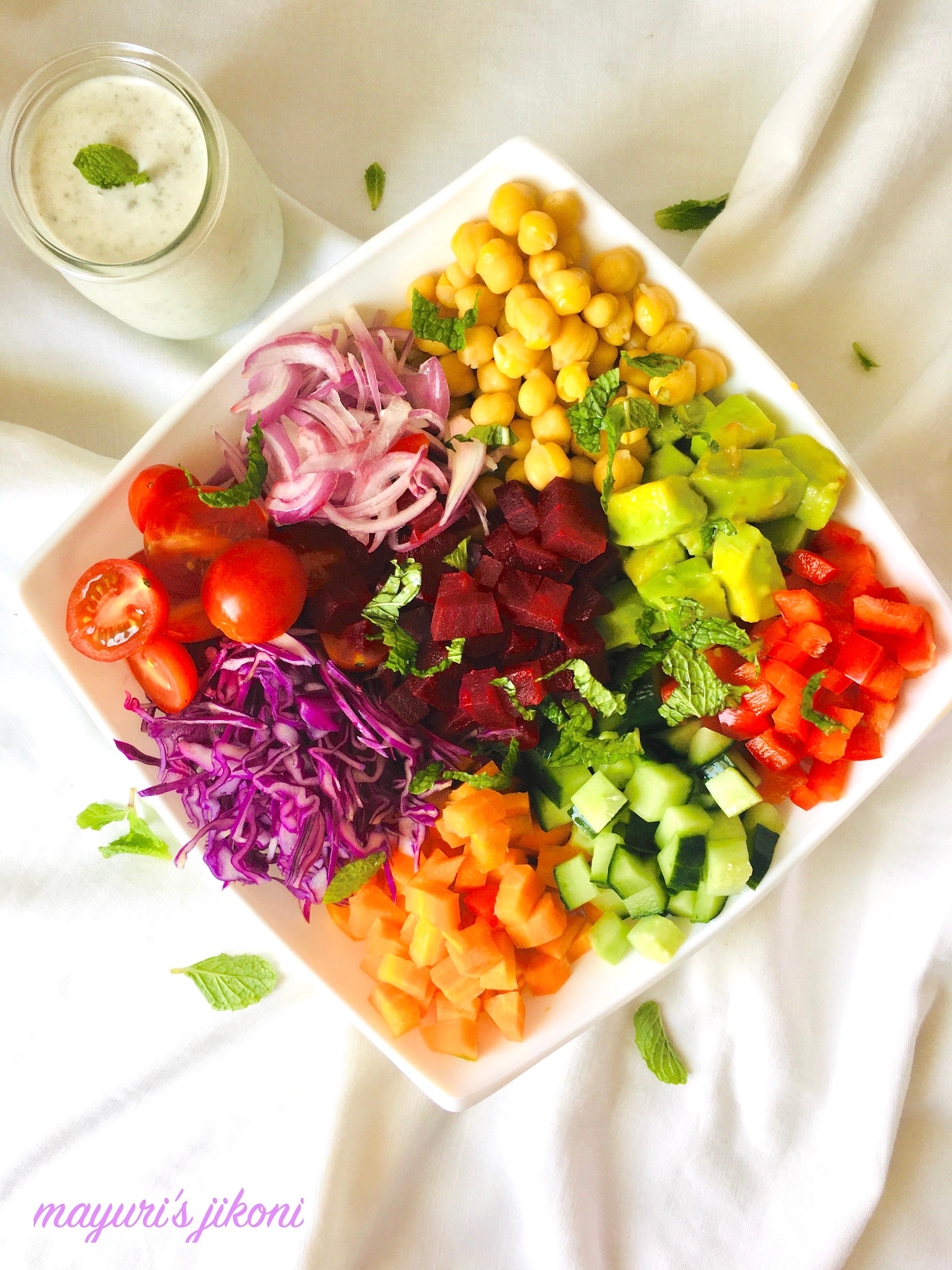 Overhead shot of a beautifully arranged healthy rainbow dinner bowl with a creamy dressing drizzle