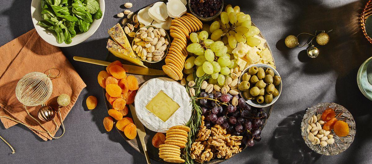Overhead shot of a rustic wooden charcuterie board with a golden-baked Camembert in the middle, surrounded by various festive charcuterie items