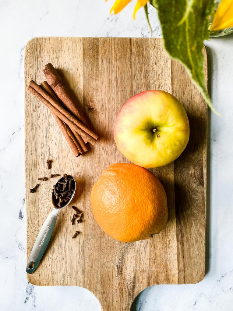 Close-up of whole oranges, cinnamon sticks, and cloves on a wooden board