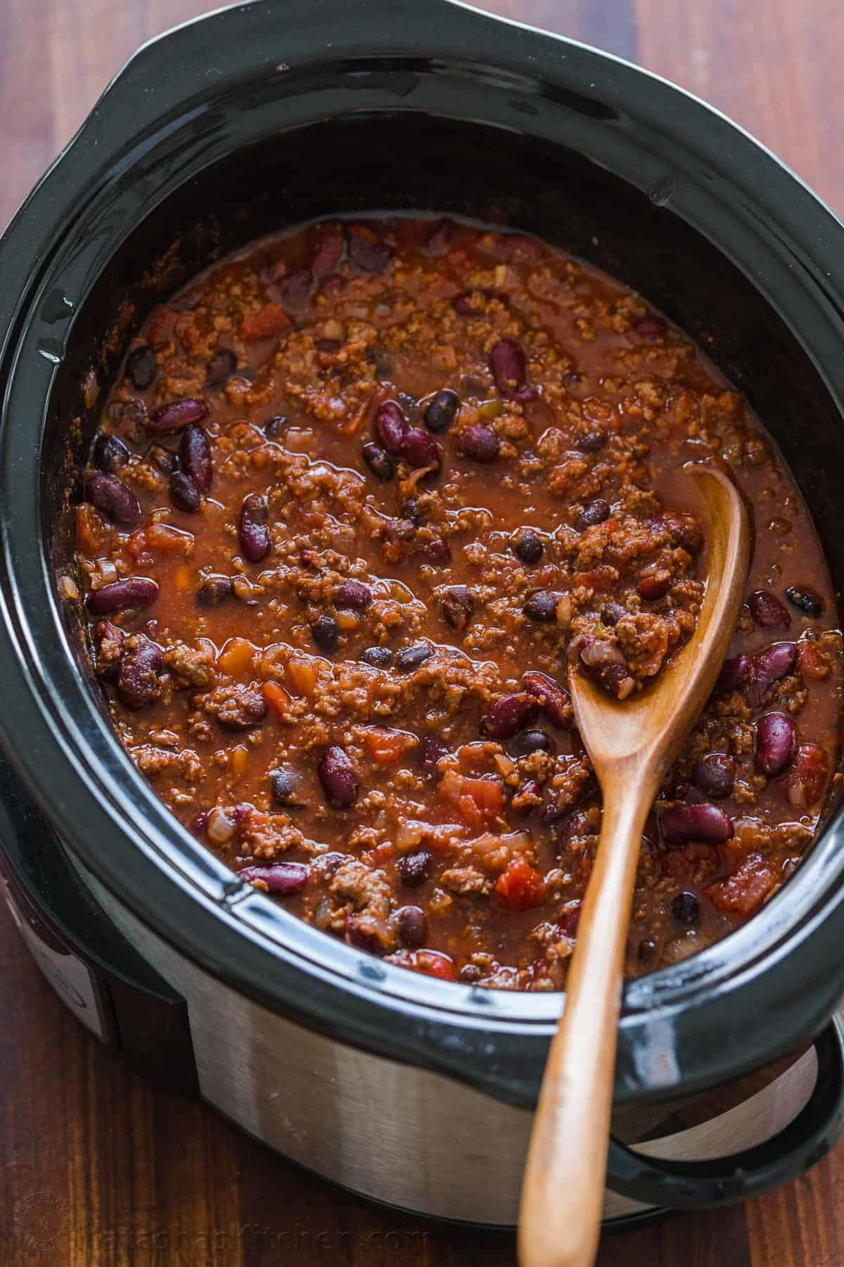 Ingredients being added to a slow cooker for chili