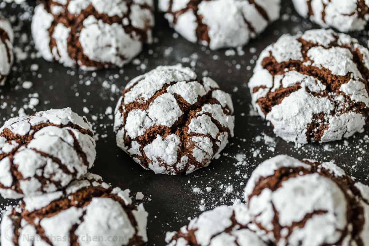 Close-up of chocolate crinkle cookie dough balls being generously rolled in powdered sugar