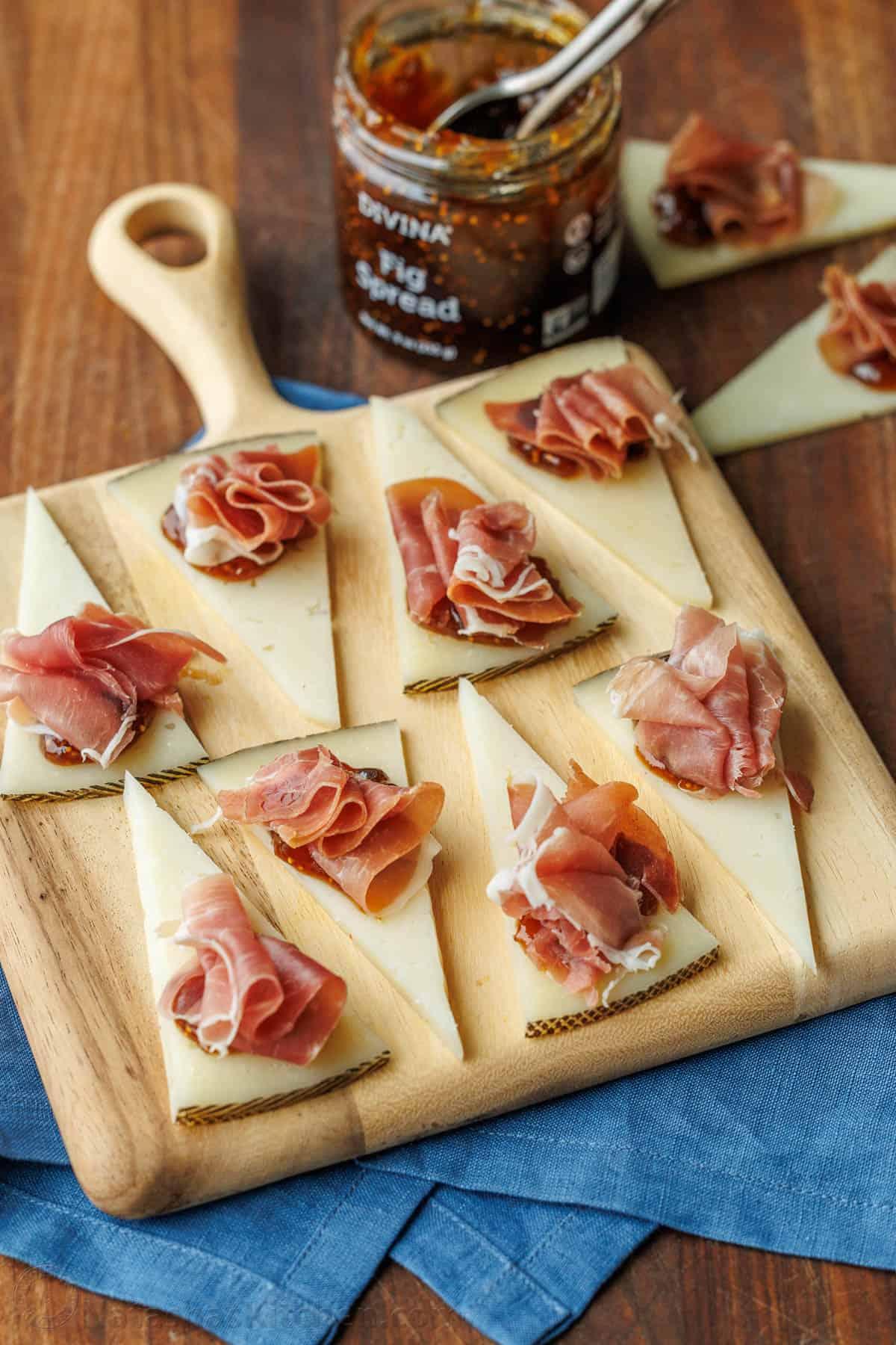Close-up of a perfectly rolled slice of prosciutto next to a dollop of fig spread on a cracker