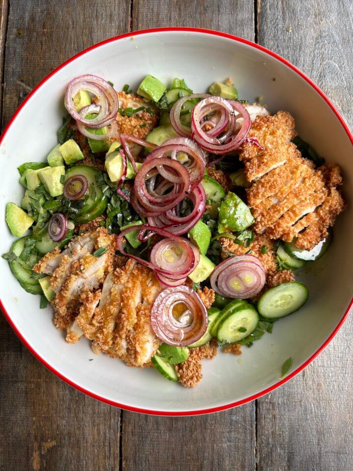 Hands tossing a fresh herb chicken bowl with a light vinaigrette