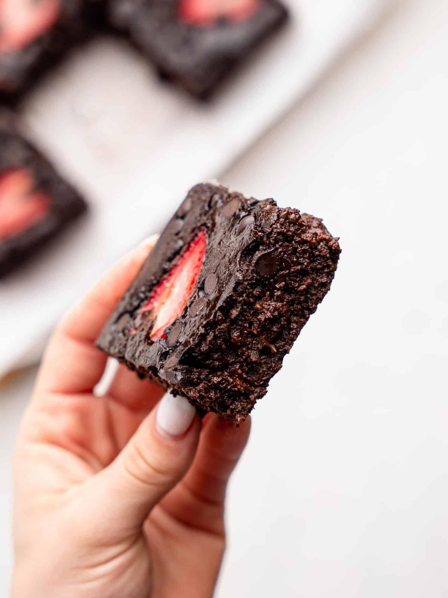 a hand holding a slice of strawberry cake brownie