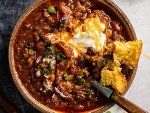 A beautifully plated serving of chili-loaded beef skillet, topped with shredded cheese and a sprig of fresh herbs, beside a glass of water.