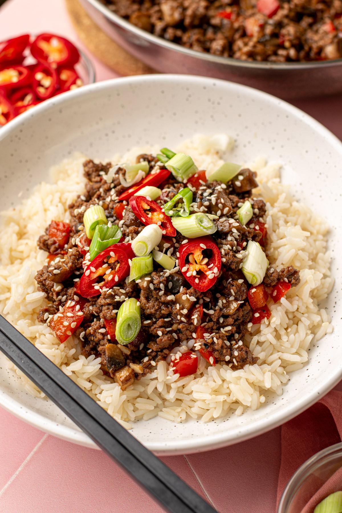 Close-up of a vibrant chili-glazed beef bowl with fresh herbs and rice, dynamic lighting, top-down view