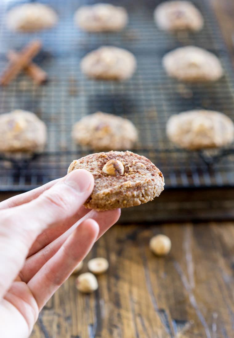 A hand reaching for a hazelnut cookie from a cooling rack, steam faintly visible.