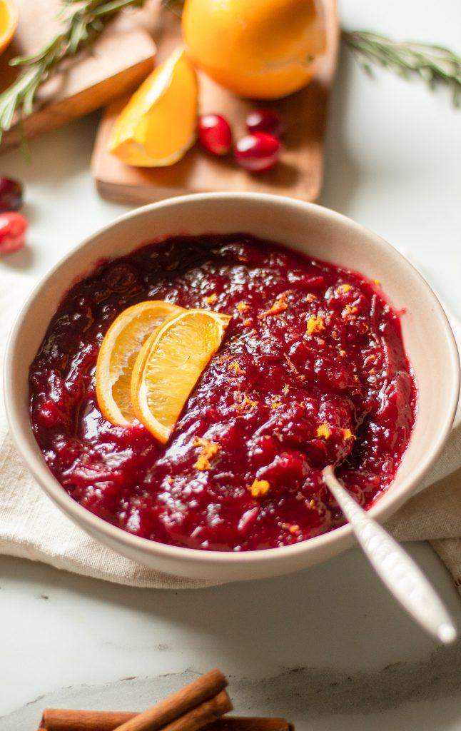 close up of cooked cranberry sauce with steam rising, garnished with orange slices