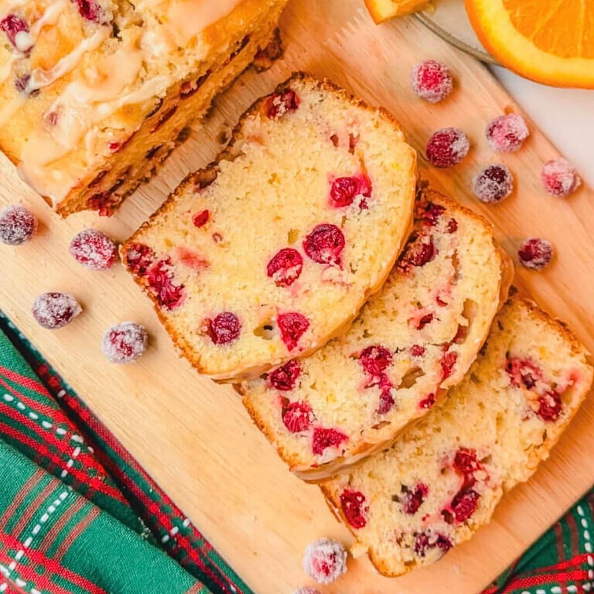 Freshly baked cranberry orange bread with white vanilla icing drizzled over top, on a rustic cutting board, natural light, cozy kitchen setting.