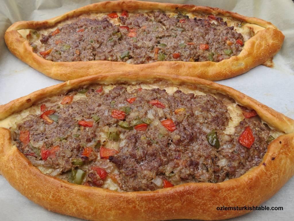 A freshly baked pide with ground meat, cheese, and vegetables, golden brown and steaming.