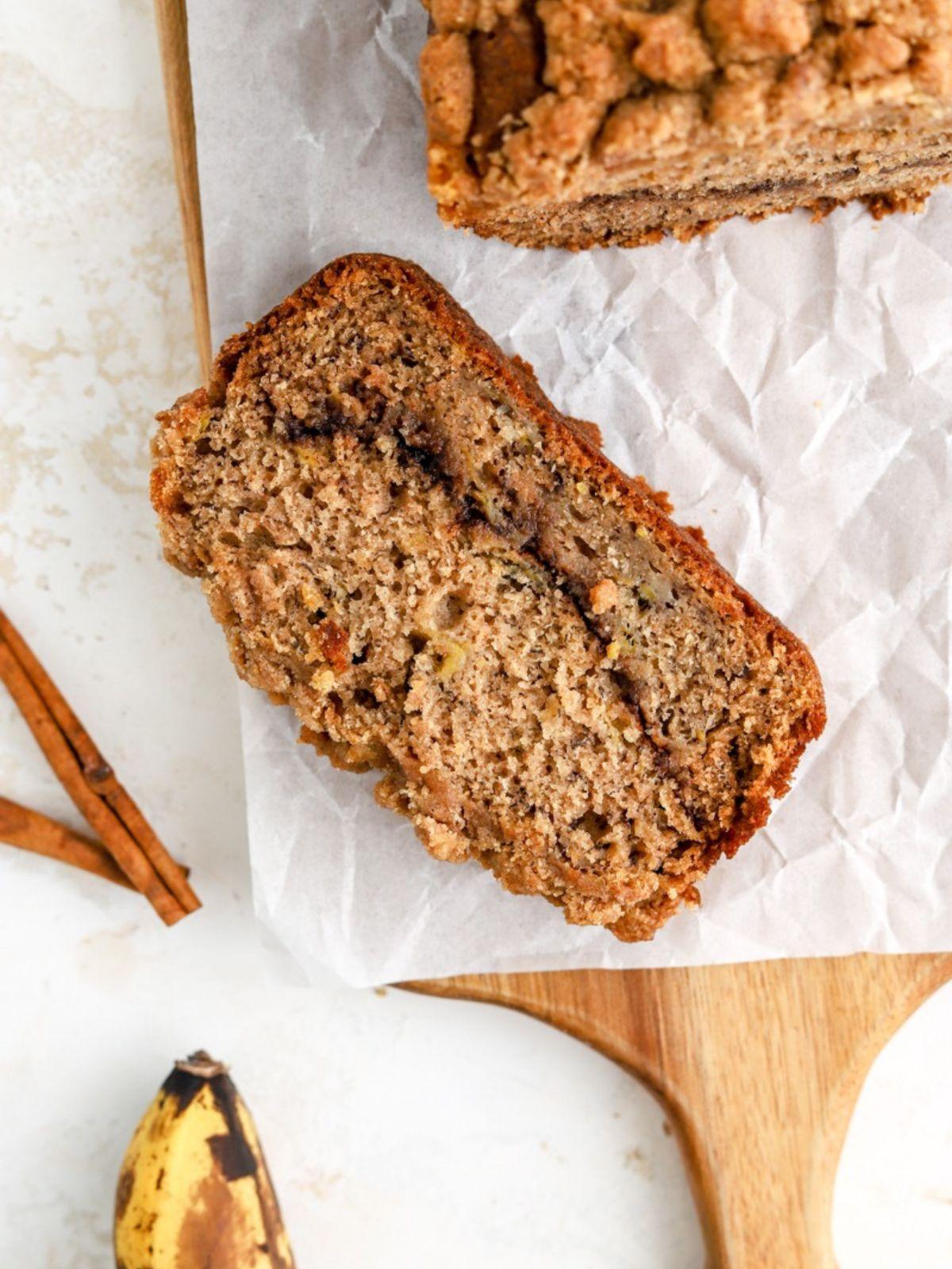 Hand pulling a warm, golden-brown slice of banana spice sugar bread from a loaf, steam visible, rustic plate