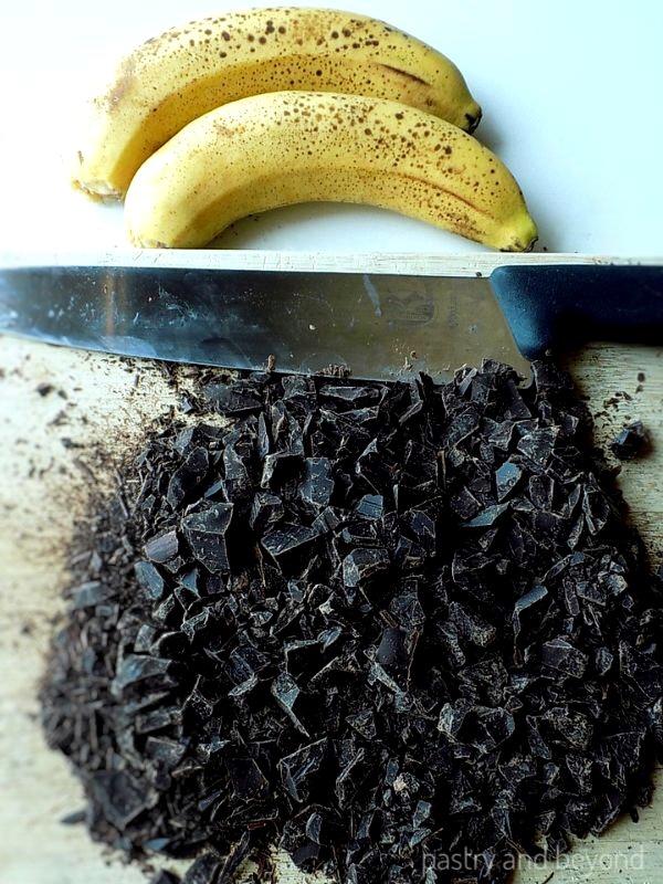 close up of mashed ripe bananas in a bowl next to a bowl of melted dark chocolate
