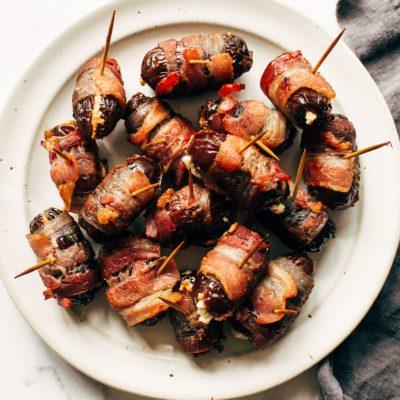 Close-up of a single bacon wrapped date on a white plate, showing the sticky glaze and crispy bacon
