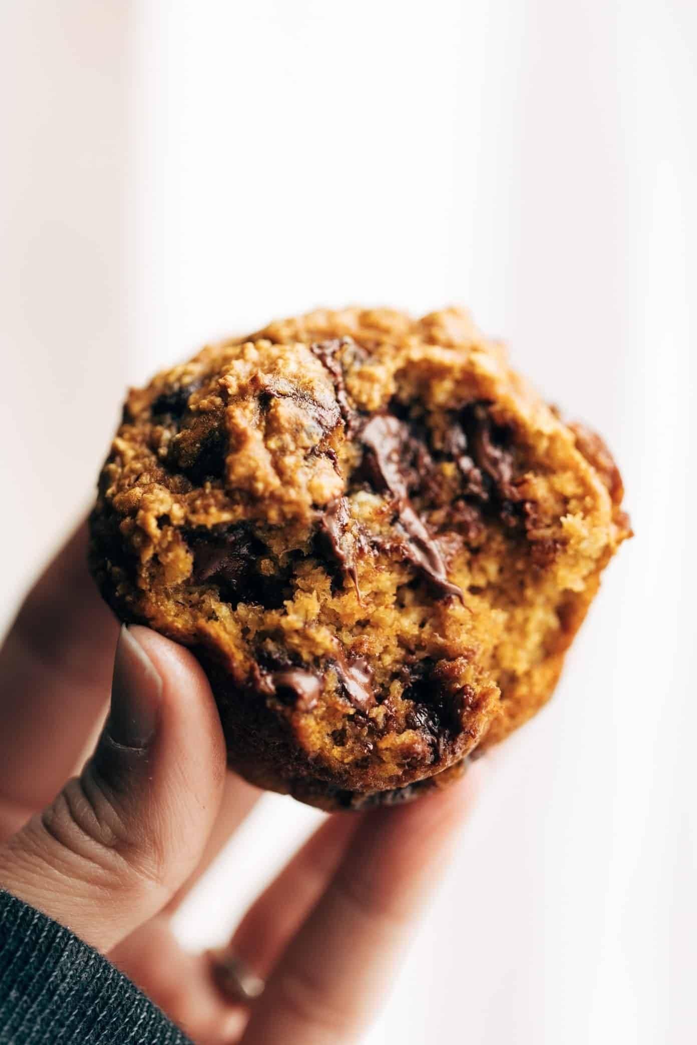 a close-up shot of a hand holding a pumpkin cinnamon muffin with a bite taken out of it