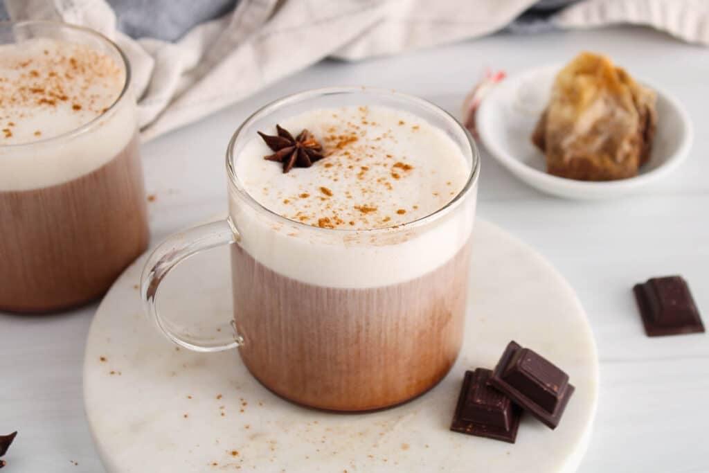 frothy chai latte being poured into a mug with chocolate syrup drizzle