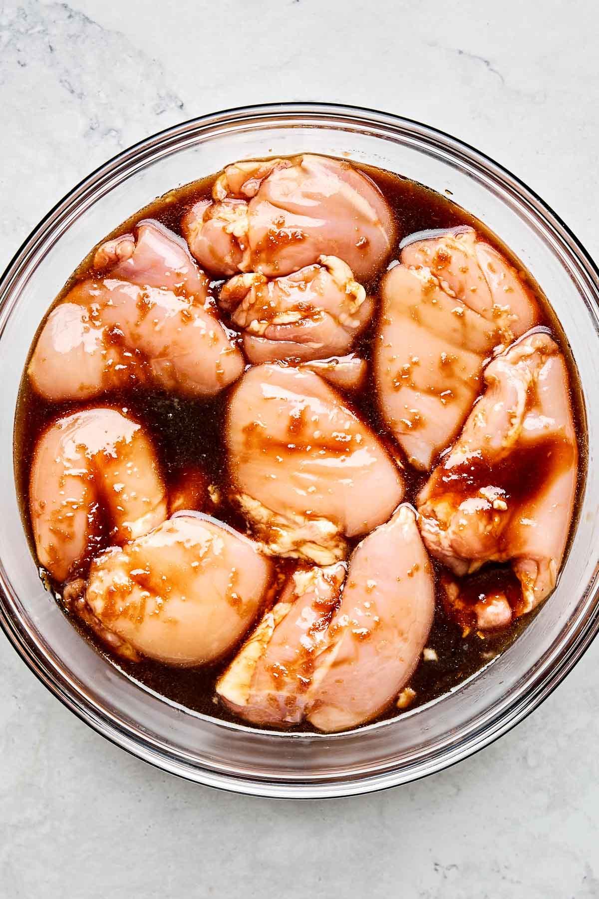 marinating chicken thighs in a bowl with teriyaki sauce
