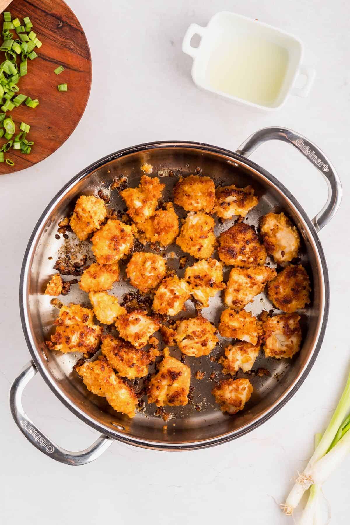 Cook preparing crispy chicken pieces in a skillet for Bang Bang Chicken Bowl