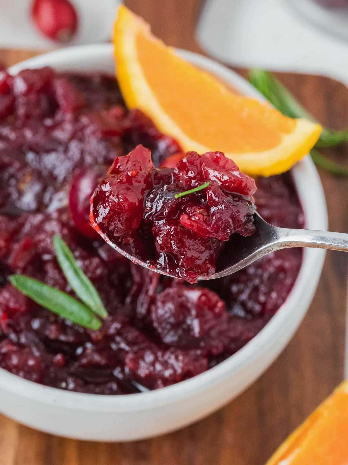 a spoonful of glistening whole berry cranberry sauce with visible orange zest over a holiday turkey slice