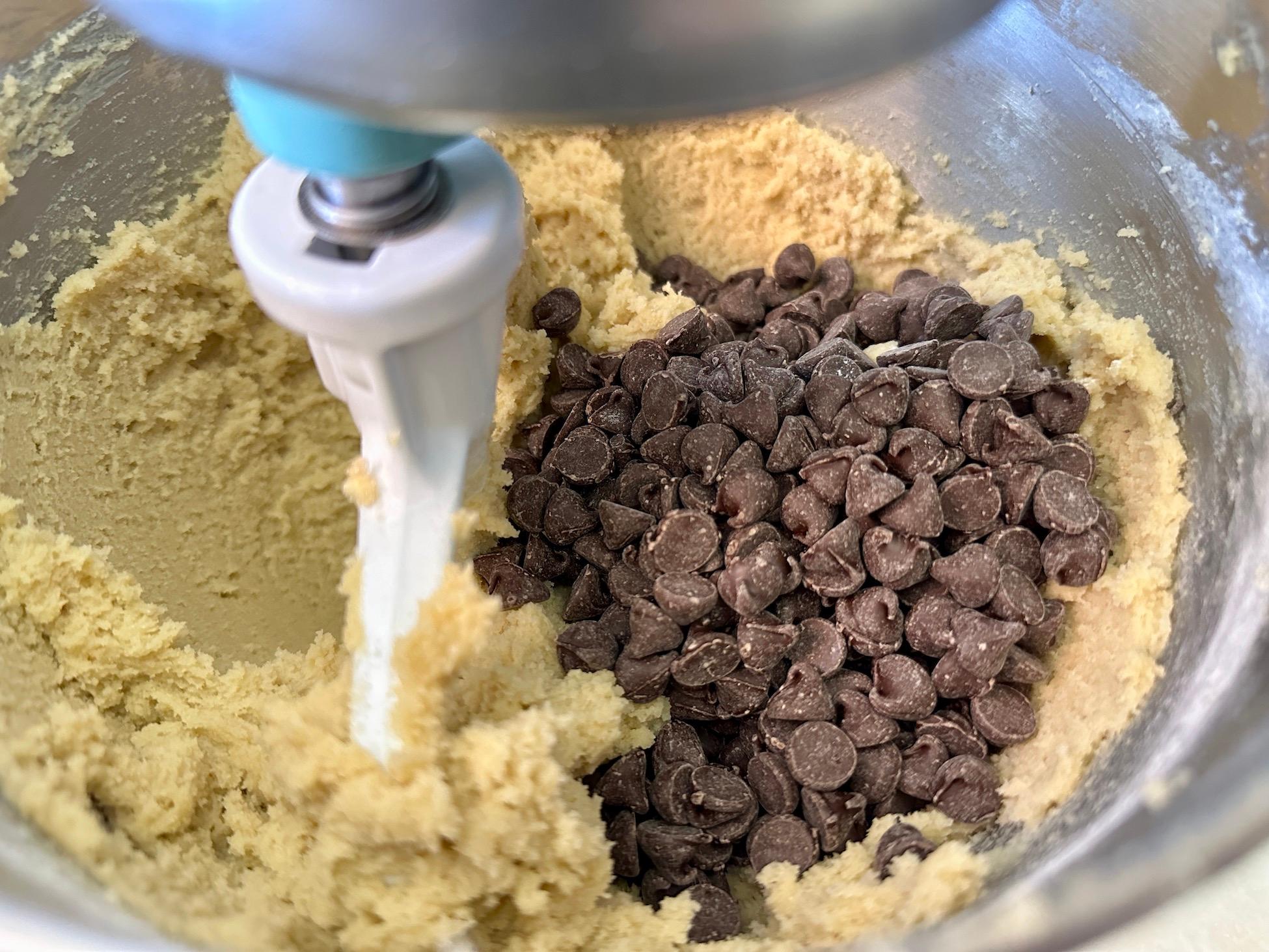 Overhead shot of cookie dough being mixed in a stand mixer, showcasing the three types of chocolate chips folded in