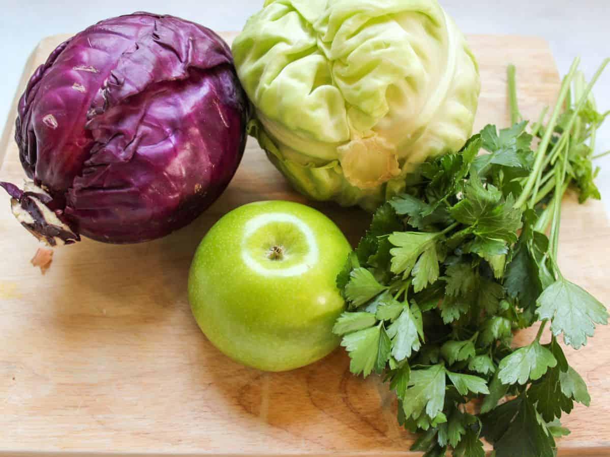 fresh red cabbage, green apples, and a bottle of red wine vinegar on a wooden cutting board