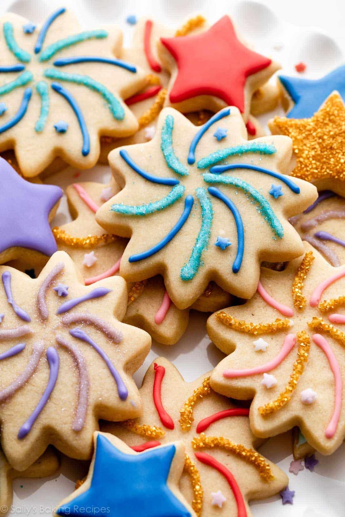 Hands decorating star cookies with various colors of glaze and sprinkles