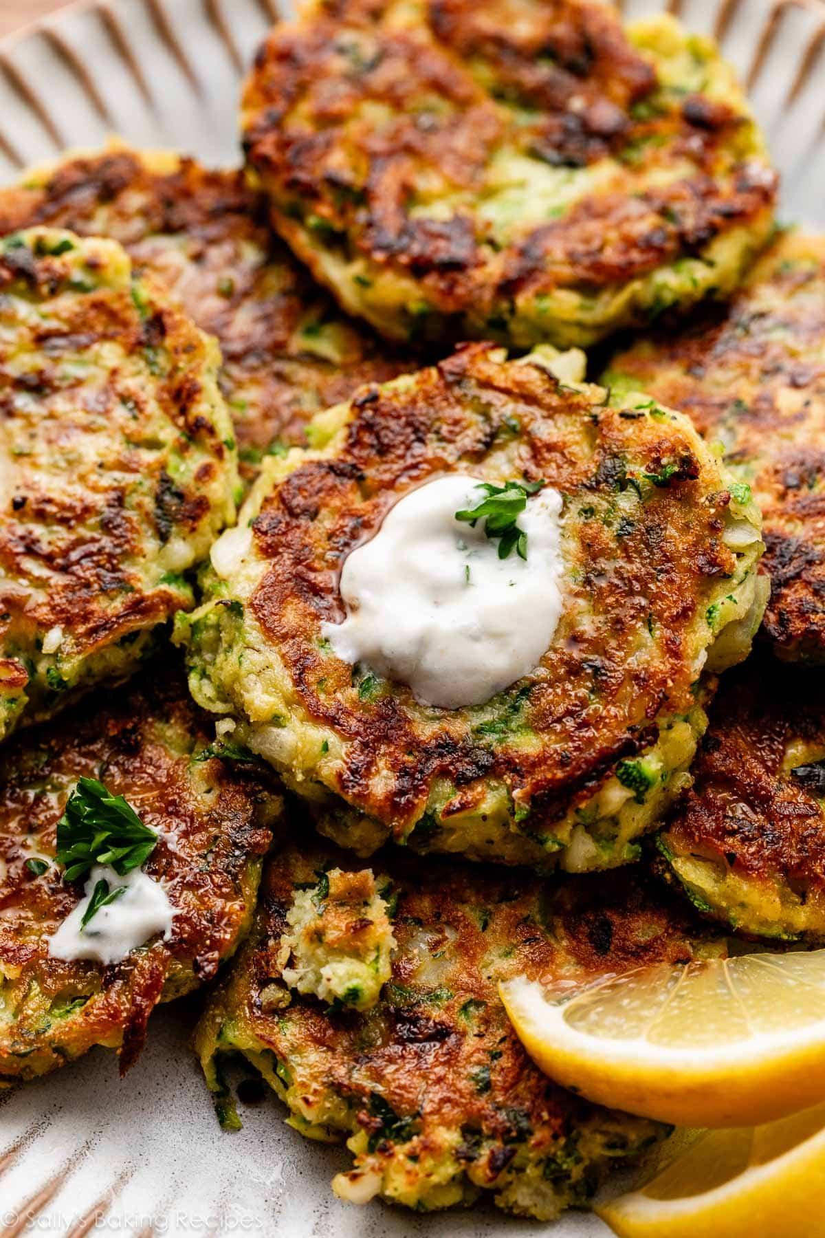 Close-up of a hand dipping a golden baked zucchini fritter into a creamy green herb yogurt sauce