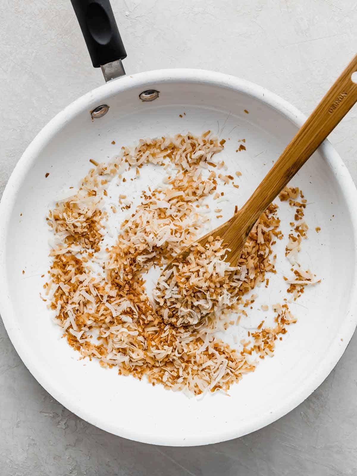 Close-up shot of unsweetened shredded coconut being lightly toasted in a dry skillet, golden brown edges