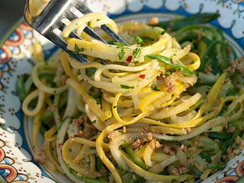 close-up of cooked zucchini noodles with golden garlic oil, parsley, and chili flakes