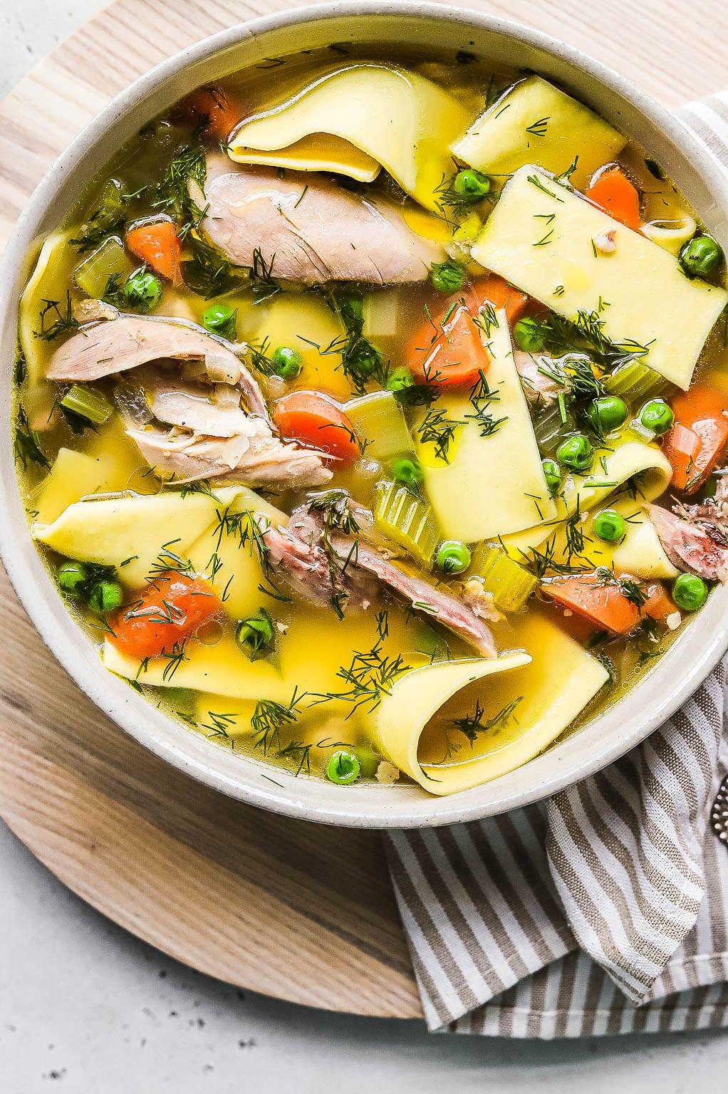 fresh herbs like parsley and dill next to a bowl of chicken noodle
