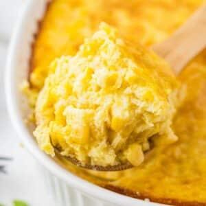 Serving spoon scooping a portion of corn casserole, showing the creamy texture