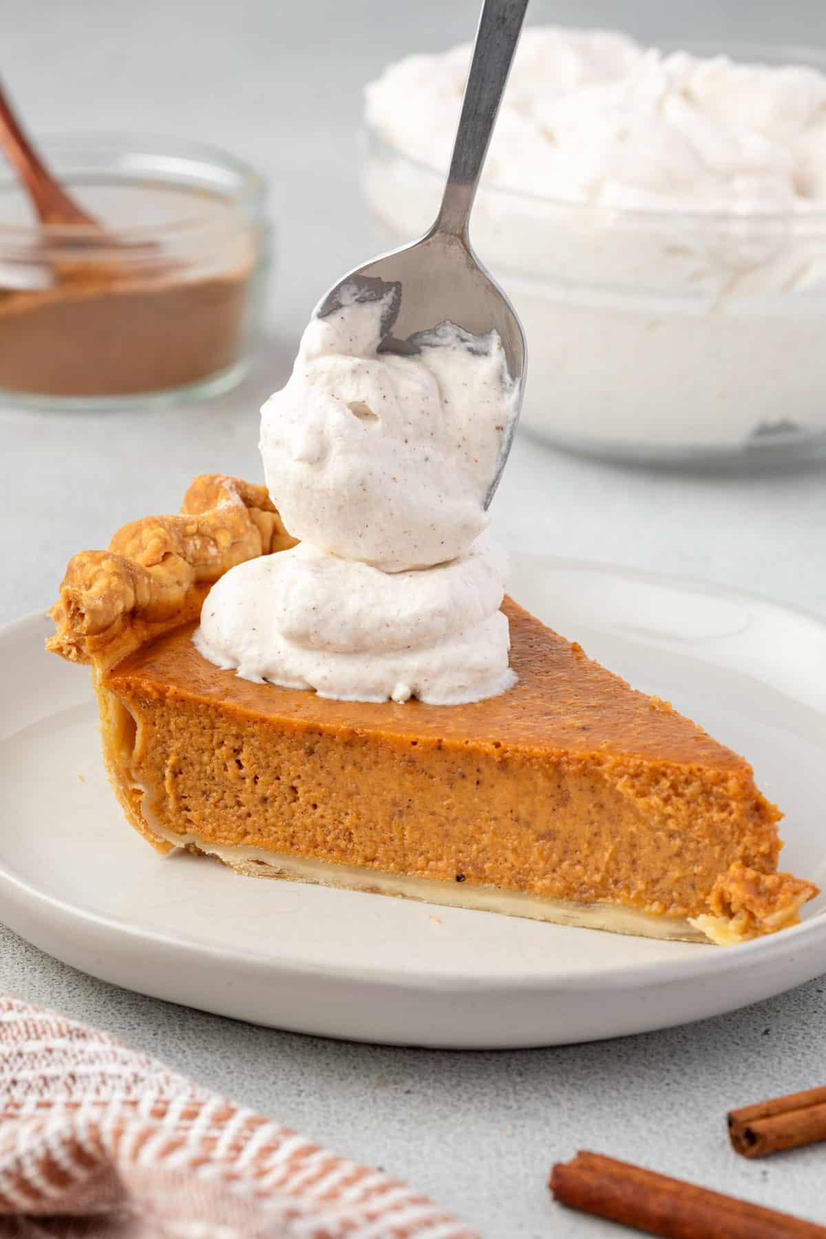 Hand holding a slice of vanilla pumpkin pie with a dollop of whipped cream