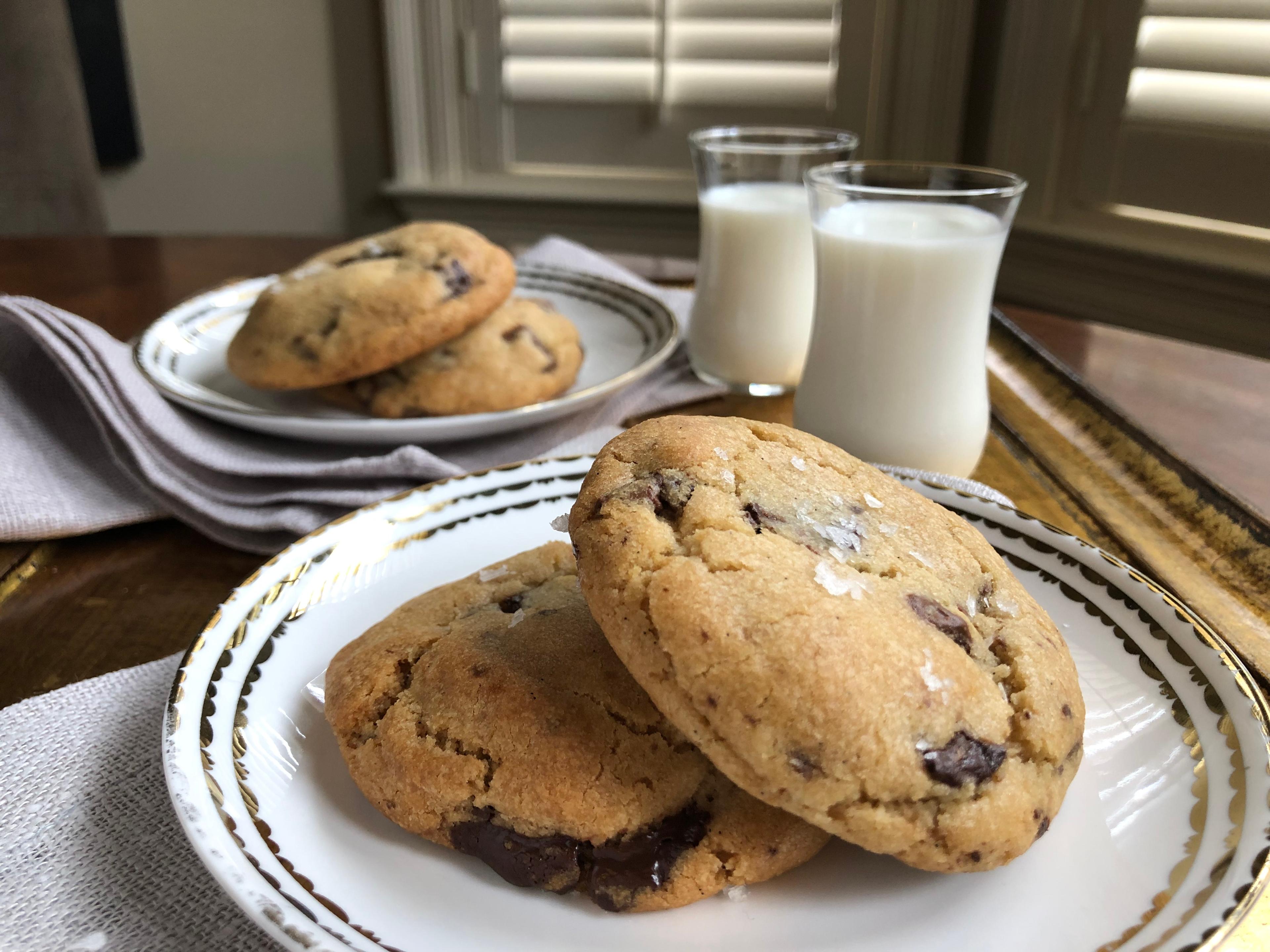 a plate of warm chocolate chip cookies with a glass of milk