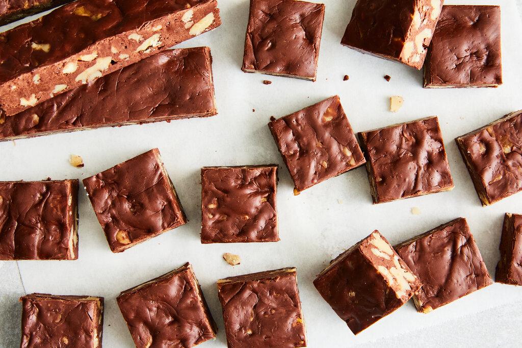 overhead shot of perfectly cut glossy chocolate fudge squares stacked on parchment paper, with a few cocoa nibs sprinkled on top